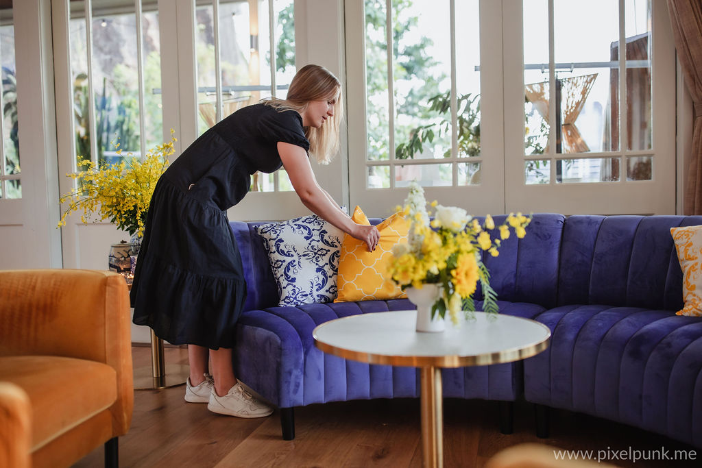 image of an event coordinator in a blue dress bending over a blue couch and straightening a yellow cushion